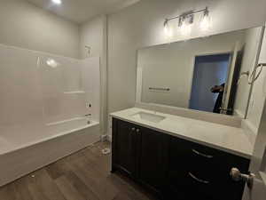 Bathroom with dark wood-type flooring, vanity, and washtub / shower combination