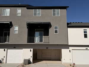 Rear view of property featuring a balcony, an attached garage, stucco siding, and driveway