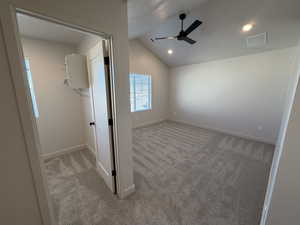 Unfurnished bedroom featuring a spacious closet, vaulted ceiling, light carpet, and a ceiling fan