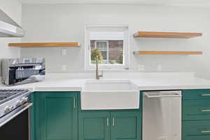 Kitchen with green cabinetry, open shelves, stainless steel appliances, and light stone counters