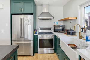 Kitchen featuring green cabinets, open shelves, stainless steel appliances, wall chimney exhaust hood, and light wood finished floors