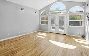 Unfurnished living room featuring french doors, vaulted ceiling, and light wood finished floors