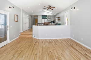 Unfurnished living room with light wood-style flooring, a ceiling fan, vaulted ceiling, recessed lighting, and plenty of natural light