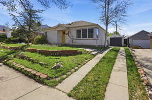 View of front of home with brick siding, an outdoor structure, a garage, and roof with shingles