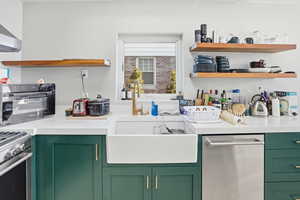 Kitchen with green cabinetry, open shelves, appliances with stainless steel finishes, and exhaust hood