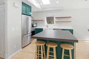 Kitchen featuring green cabinets, light wood-style floors, a breakfast bar, stainless steel appliances, and a center island