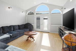 Living room with french doors, light wood-style floors, high vaulted ceiling, and recessed lighting