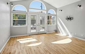 Unfurnished living room featuring french doors, vaulted ceiling, and light wood-style floors