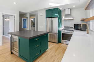 Kitchen with green cabinets, stainless steel appliances, wine cooler, recessed lighting, and open shelves