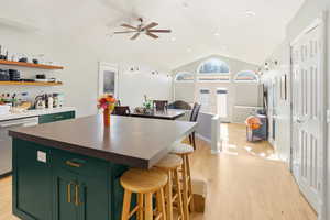 Kitchen featuring green cabinetry, vaulted ceiling, a center island, dishwasher, and a breakfast bar area