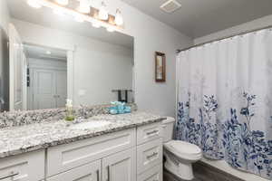Full bathroom featuring vanity, curtained shower, and dark wood-style flooring next to the two extra bedrooms