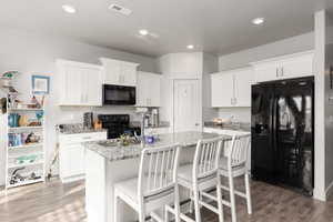 Kitchen with black appliances, white cabinetry, light stone counters, a breakfast bar area, and recessed lighting