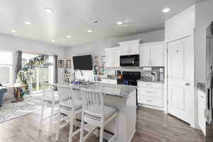 Kitchen with a center island with sink, white cabinetry, a breakfast bar, light stone counters, and black appliances