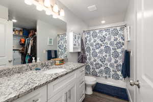 Full bath with vanity, dark wood-style flooring, shower / bath combination with curtain, and a walk in closet
