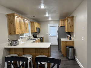 Kitchen featuring a peninsula, light countertops, stainless steel appliances, a breakfast bar area, and dark wood-style flooring