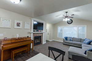 Living area featuring a brick fireplace, vaulted ceiling, and a ceiling fan