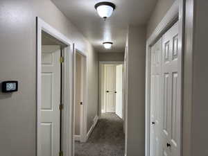 Hallway with dark colored carpet and baseboards