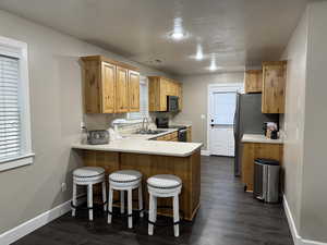 Kitchen with a peninsula, light countertops, stainless steel appliances, a kitchen bar, and dark wood-style flooring