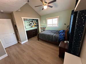 Bedroom with a textured ceiling, ceiling fan, light wood finished floors, and lofted ceiling