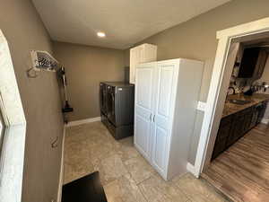 Laundry room featuring light tile patterned floors, a textured ceiling, independent washer and dryer, and cabinet space