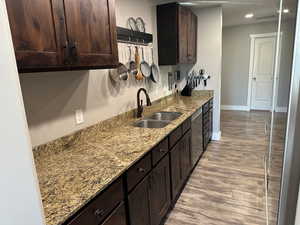 Kitchen featuring dark brown cabinets, light stone countertops, light wood-style floors, dishwasher, and recessed lighting