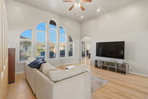 Living room with light wood-style flooring, arched walkways, ceiling fan, recessed lighting, and a high ceiling