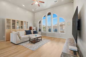 Living room with light wood-style floors, a towering ceiling, recessed lighting, and a ceiling fan