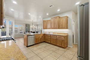 Kitchen featuring appliances with stainless steel finishes, light stone countertops, a chandelier, light tile patterned flooring, and a peninsula