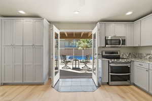Kitchen with appliances with stainless steel finishes, light stone counters, light wood-type flooring, recessed lighting, and gray cabinets
