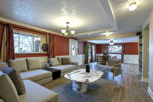 Living room featuring a textured ceiling, wood finished floors, wainscoting, a chandelier, and ornamental molding