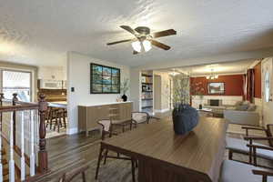 Dining space featuring a textured ceiling, a chandelier, wood finished floors, ceiling fan, and wainscoting