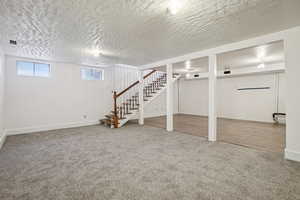 Below grade area with carpet flooring, a textured ceiling, and stairs