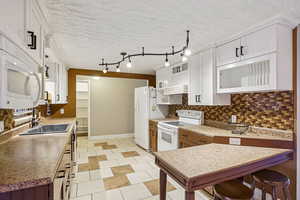 Kitchen featuring white appliances, backsplash, a textured ceiling, light countertops, and white cabinetry