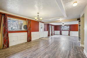Unfurnished dining area with a wainscoted wall, a chandelier, a textured ceiling, wood finished floors, and a decorative wall