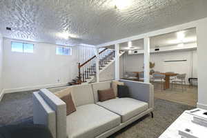 Carpeted living room featuring a textured ceiling and stairs
