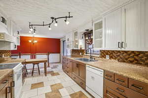 Kitchen with white cabinets, a textured ceiling, glass insert cabinets, brown cabinets, and hanging light fixtures