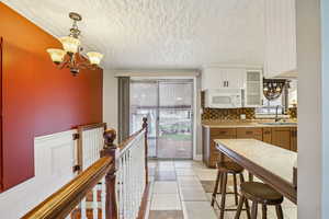 Kitchen featuring brown cabinets, a textured ceiling, a chandelier, white cabinetry, and decorative light fixtures