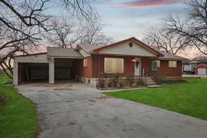 Ranch-style home featuring a yard, driveway, brick siding, covered porch, and a shingled roof