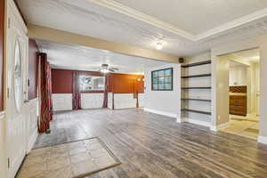 Unfurnished living room with a textured ceiling, wood finished floors, healthy amount of natural light, ornamental molding, and a wainscoted wall