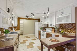 Kitchen featuring white appliances, tasteful backsplash, white cabinets, light countertops, and a textured ceiling