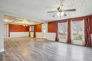 Unfurnished living room featuring a wainscoted wall, wood finished floors, a textured ceiling, a chandelier, and a ceiling fan
