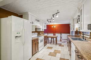 Kitchen featuring white appliances, a textured ceiling, wainscoting, light countertops, and white cabinets