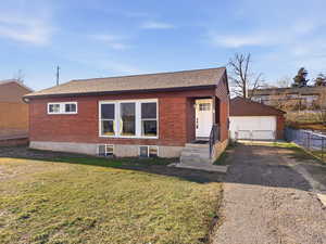 Ranch-style home featuring roof with shingles, brick siding, a gate, and an outbuilding