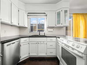 Kitchen with white electric stove, stainless steel dishwasher, white cabinets, and crown molding