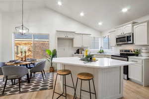 Kitchen with a breakfast bar, stainless steel appliances, white cabinetry, a center island, and light wood-type flooring