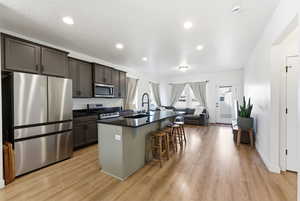 Kitchen featuring appliances with stainless steel finishes, a kitchen island with sink, a kitchen bar, open floor plan, and light wood-style flooring
