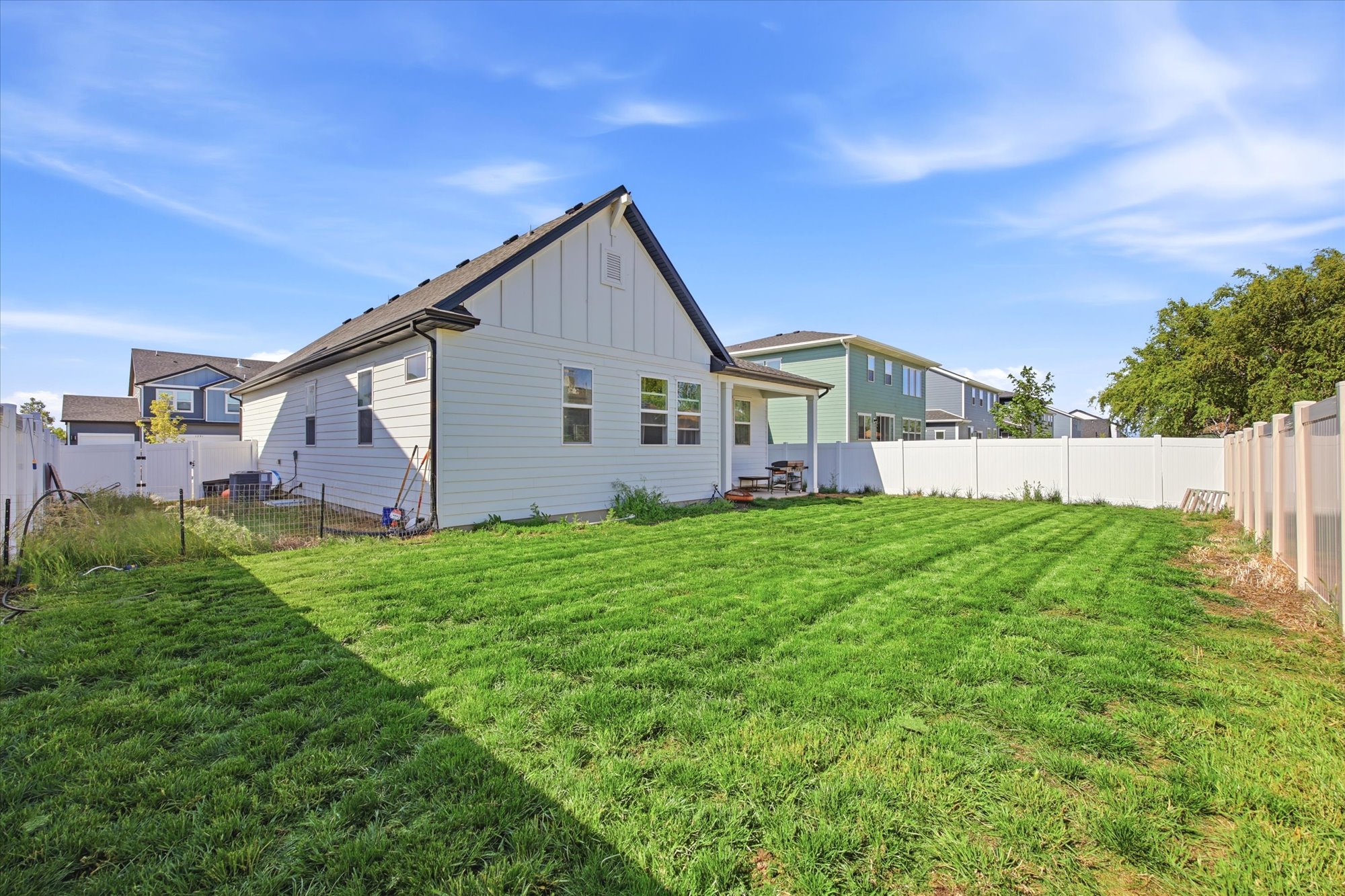 Spacious backyard featuring a rectangular lawn, white vinyl fencing, and a light-colored exterior with a black roof