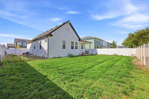 Spacious backyard featuring a rectangular lawn, white vinyl fencing, and a light-colored exterior with a black roof