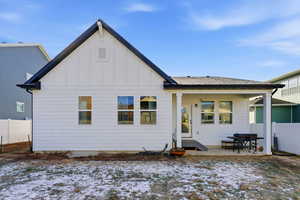 Snow covered rear of property featuring board and batten siding, a patio, and a shingled roof