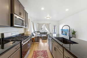 Kitchen featuring appliances with stainless steel finishes, dark stone counters, open floor plan, light wood-style floors, and recessed lighting
